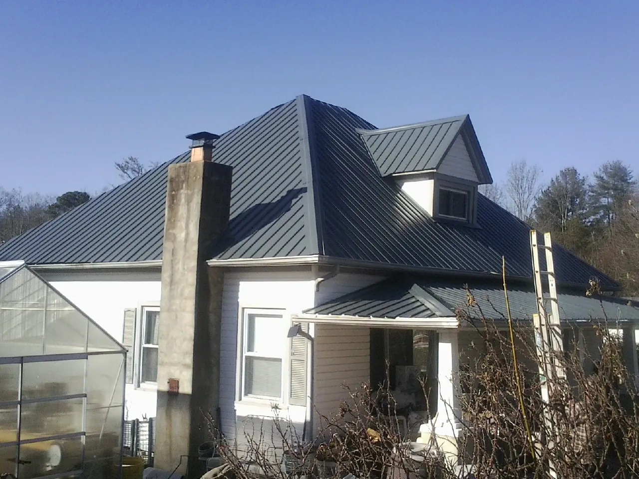 Dark blue standing seam metal roof on a white farmhouse with dormer — Slate & Tile Roof Repair by Roofing Brothers in Johnson