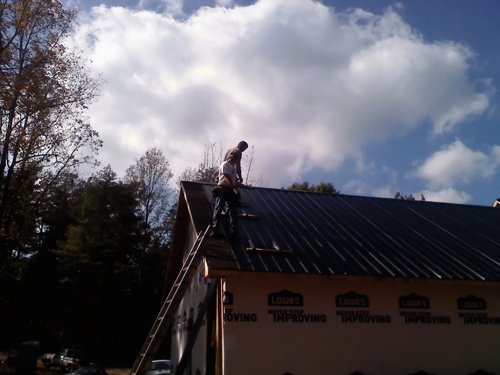 Roofer fastening dark metal panels high against a cloudy sky, from a Roof Inspection job in Johnson